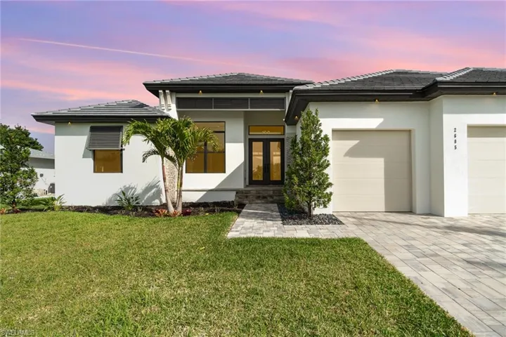 Prairie-style home with french doors, stucco siding, a lawn, decorative driveway, and a garage