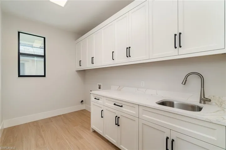Massive laundry room with lots of cabinetry, undermount laundry sink and light wood plank tile flooring