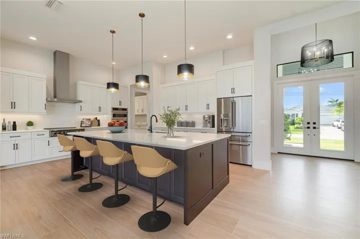 Kitchen featuring white cabinetry, pendant lighting, french doors, an island with sink, and recessed lighting
