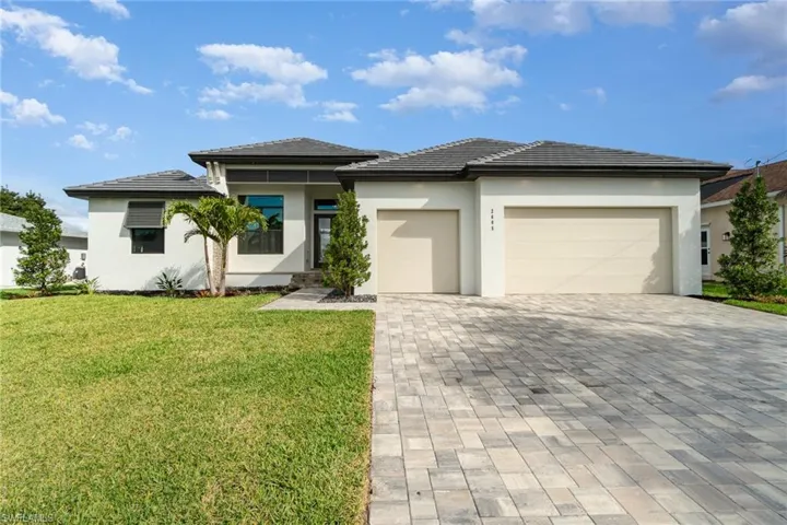 Prairie-style home with an attached garage, decorative driveway, stucco siding, and a front lawn