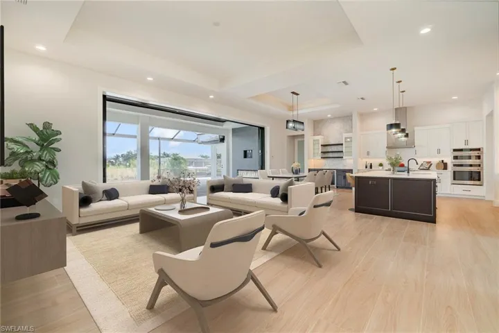 Living room with a raised ceiling, light wood plank tile floors, and recessed lighting