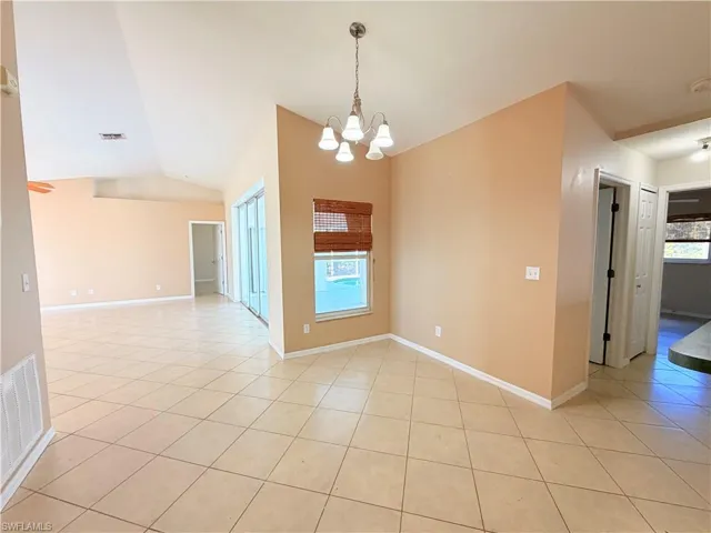 Empty room with hanging lights, light tile patterned floors, and lofted ceiling