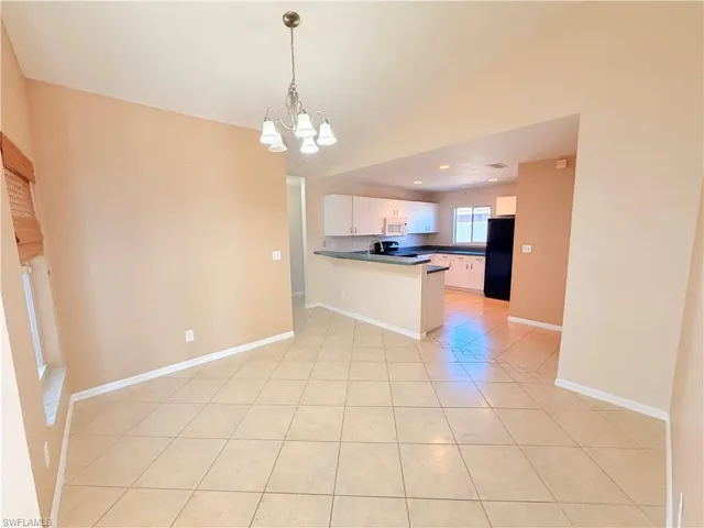 Kitchen with dark countertops, a peninsula, light tile patterned flooring, a chandelier, and freestanding refrigerator