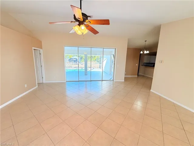 Unfurnished room with a ceiling fan, vaulted ceiling, light tile patterned flooring, and a chandelier