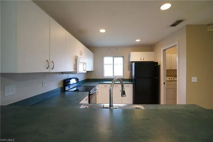 Kitchen with dark countertops, black appliances, white cabinets, washer / dryer, and recessed lighting