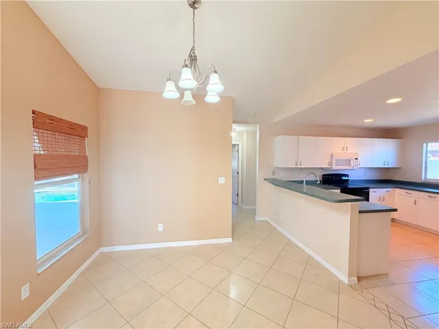 Kitchen with dark countertops, a peninsula, white cabinetry, black range with electric stovetop, and suspended lighting