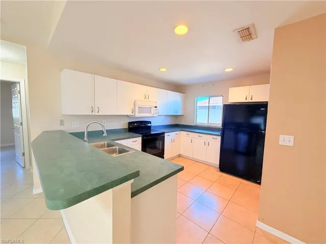 Kitchen featuring black appliances, a peninsula, dark countertops, white cabinetry, and recessed lighting