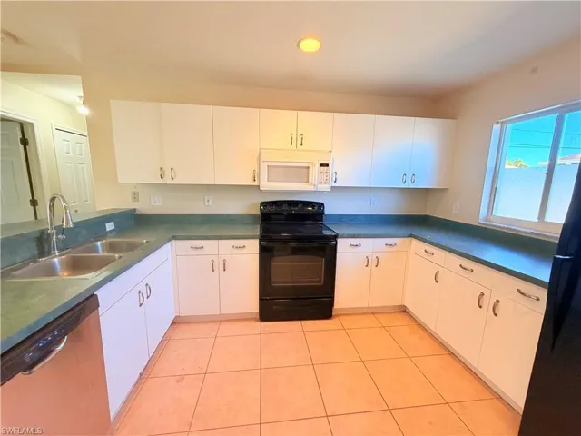 Kitchen with black appliances, dark countertops, white cabinetry, light tile patterned floors, and recessed lighting