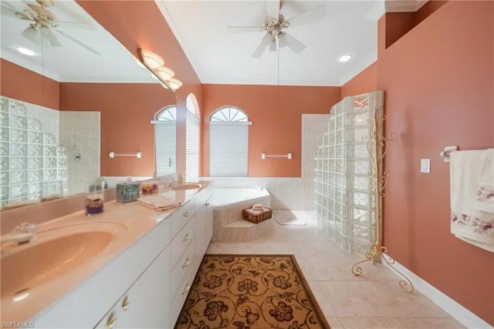 Bathroom featuring tile patterned flooring, ceiling fan, tiled bath, and double sink vanity