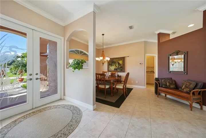 Foyer with an inviting chandelier, french doors, light tile patterned floors, and ornamental molding