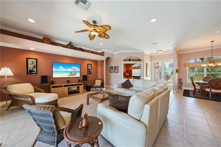 Living room featuring ornamental molding, ceiling fan with notable chandelier, light tile patterned floors, and french doors