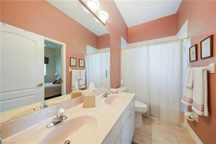 Full bathroom featuring shower / bath combo with shower curtain, toilet, tile patterned flooring, and double vanity