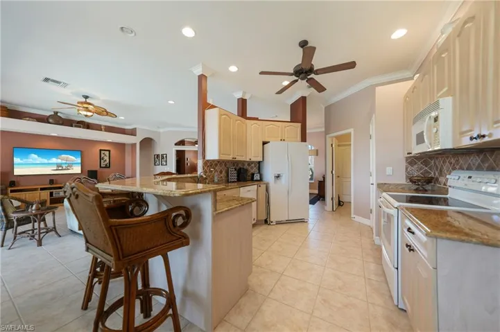 Kitchen featuring light tile patterned floors, ceiling fan, decorative backsplash, white appliances, and kitchen peninsula