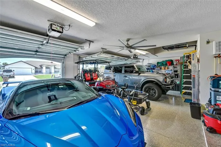Spacious 3 car garage featuring a finished epoxy floor, large ceiling fan, and multiple overhead fluorescent light fixtures