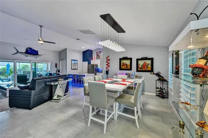 Open-concept interior featuring light gray tile flooring, a contemporary linear chandelier, vaulted ceilings, and extensive sliding glass doors