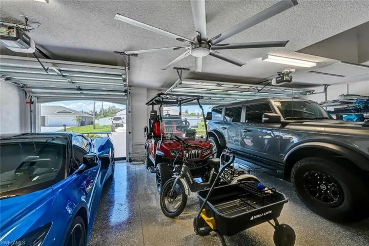 Spacious 3 car garage featuring an epoxy-coated floor, multiple automatic garage doors, and a large ceiling fan