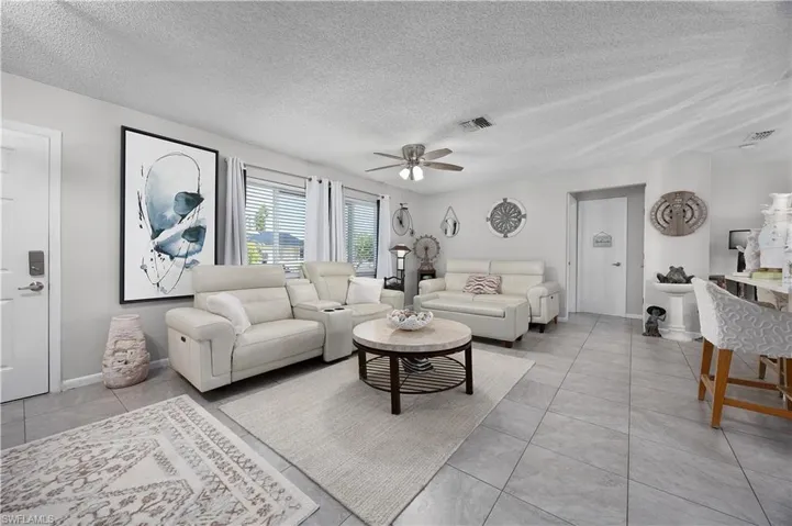 Living area with a textured ceiling, light tile patterned floors, and ceiling fan