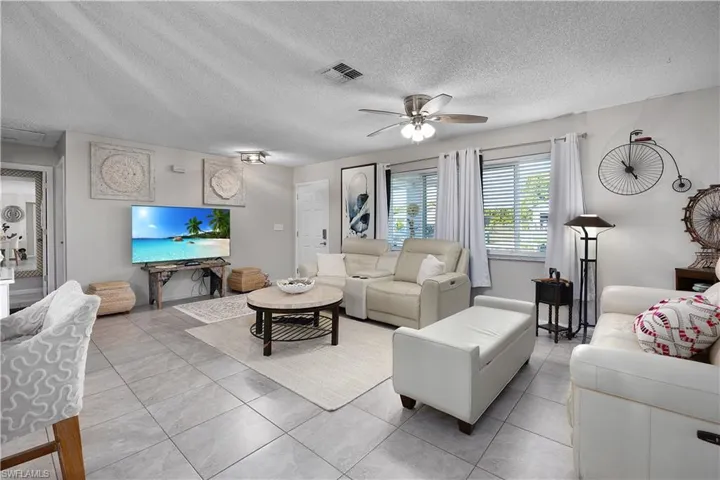 Living room with a textured ceiling, tile patterned flooring, and a ceiling fan