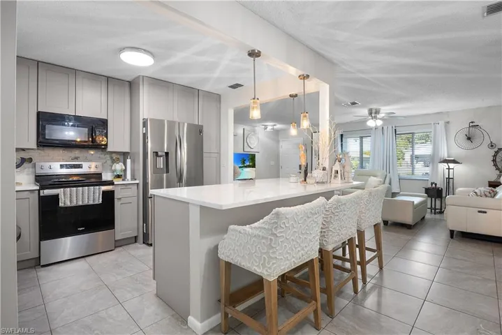Kitchen with gray cabinetry, stainless steel appliances, open floor plan, hanging light fixtures, and a kitchen bar