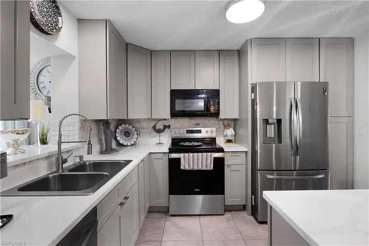 Kitchen with gray cabinetry, stainless steel appliances, tasteful backsplash, light stone countertops, and light tile patterned floors