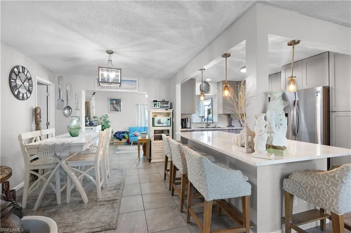 Kitchen featuring gray cabinetry, a textured ceiling, stainless steel fridge with ice dispenser, hanging light fixtures, and a kitchen breakfast bar