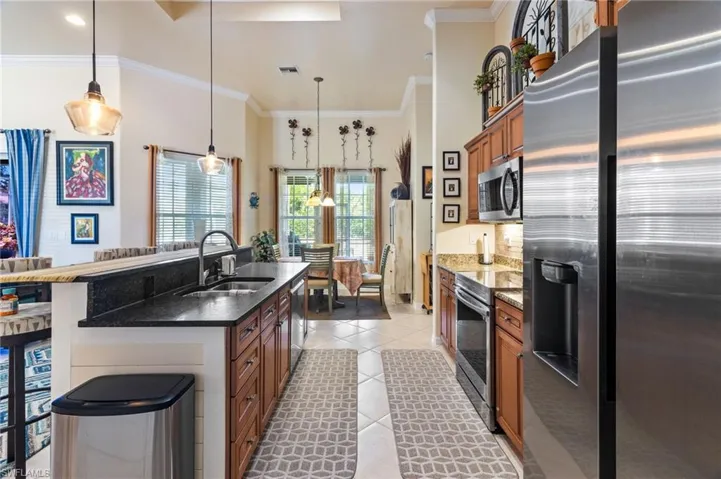 Kitchen with light tile flooring, a center island with sink, dark stone countertops, appliances with stainless steel finishes, and sink