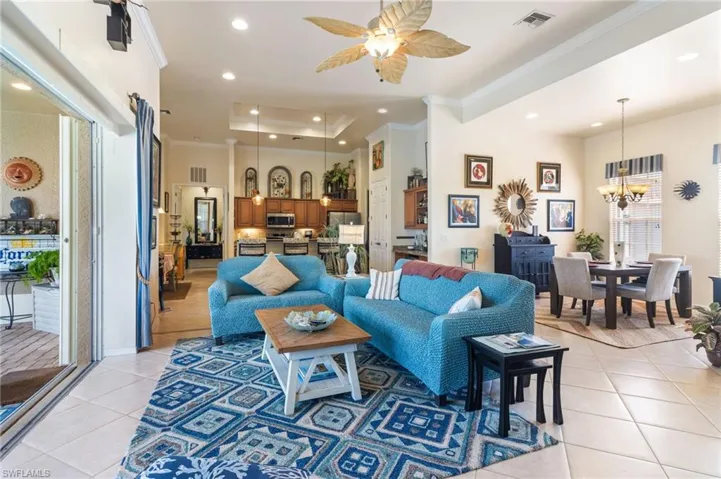 Tiled living room with a tray ceiling, crown molding, and ceiling fan with notable chandelier