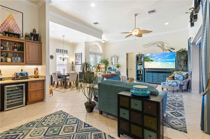 Tiled living room with beverage cooler, ornamental molding, and ceiling fan