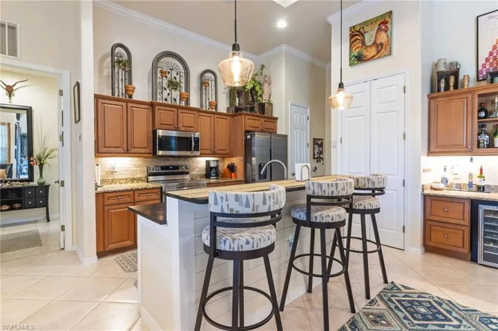 Kitchen featuring light tile flooring, stainless steel appliances, hanging light fixtures, a kitchen island with sink, and light stone countertops