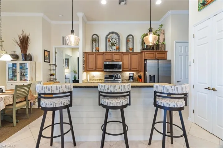 Kitchen featuring a breakfast bar area, appliances with stainless steel finishes, light tile floors, and decorative light fixtures