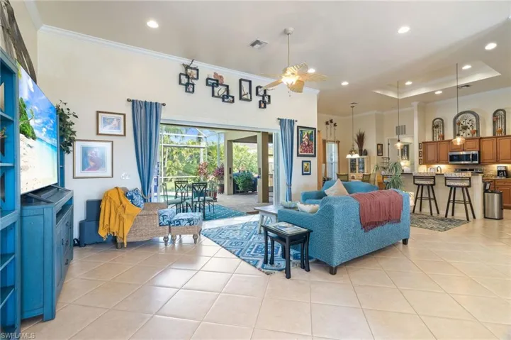 Living room with ceiling fan, a tray ceiling, light tile floors, and crown molding