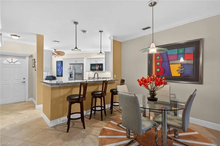 The property features a kitchen with white cabinetry and stainless steel appliances, a breakfast bar with pendant lighting, and a dining area with a glass table and upholstered chairs