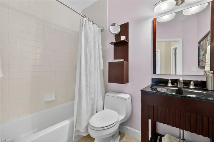 Bathroom featuring a bathtub with tiled walls, a toilet, and a vanity with a dark countertop and a mirror