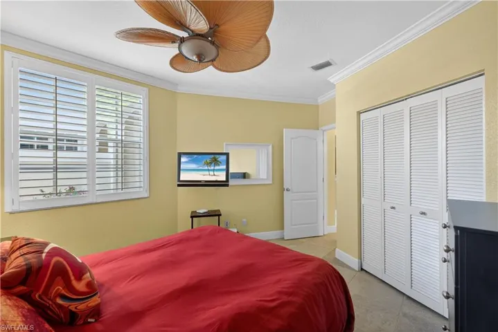 This room features a ceiling fan with natural-toned blades, a window with white plantation shutters, and a closet with louvered bifold doors