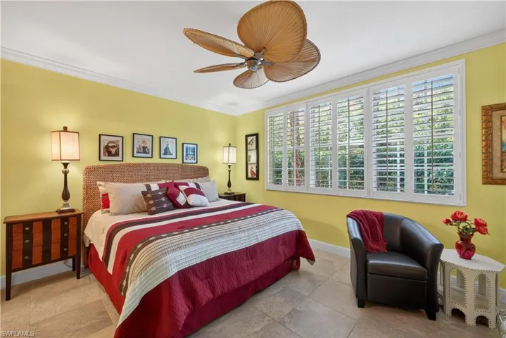 This bedroom features light yellow walls, tile flooring, and a ceiling fan with palm-leaf style blades