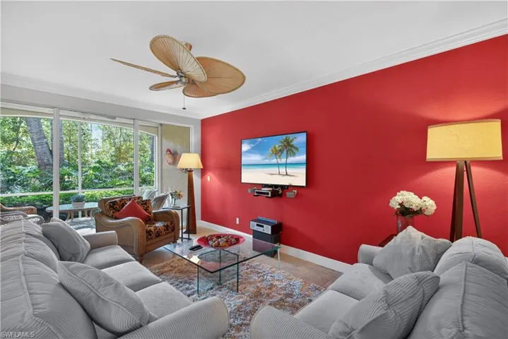 The living area features a bright red accent wall, a ceiling fan, and large windows with views of abundant greenery