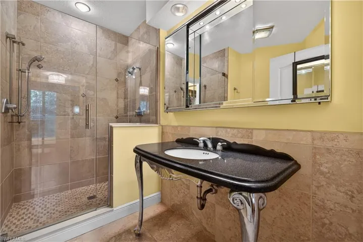 Well-appointed bathroom featuring a glass-enclosed shower with tiled walls and floor, a vanity with a dark countertop and white basin, and a large mirror with integrated lighting