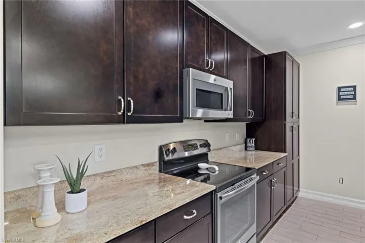 Kitchen featuring dark brown cabinets, light stone countertops, stainless steel appliances, and light wood-type flooring