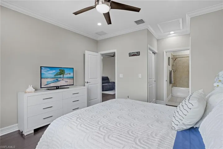 Bedroom with connected bathroom, ornamental molding, dark hardwood / wood-style flooring, and ceiling fan