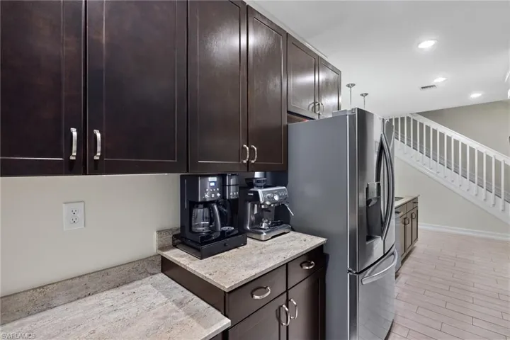 Kitchen featuring light stone counters, dark brown cabinets, stainless steel fridge, and light hardwood / wood-style floors