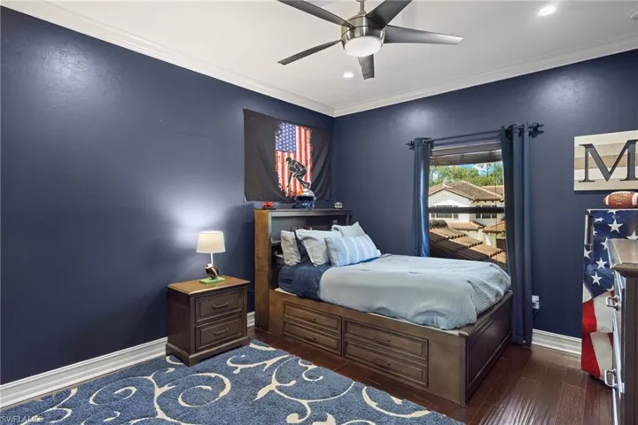 Bedroom with ornamental molding, dark wood-type flooring, and ceiling fan