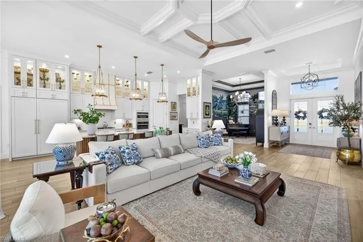 Living room with light wood-style floors, coffered ceiling, a chandelier, crown molding, and a ceiling fan