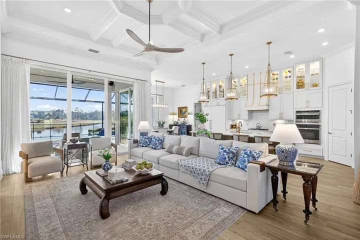Living room featuring coffered ceiling, ornamental molding, a ceiling fan, suspended lighting, and a water view