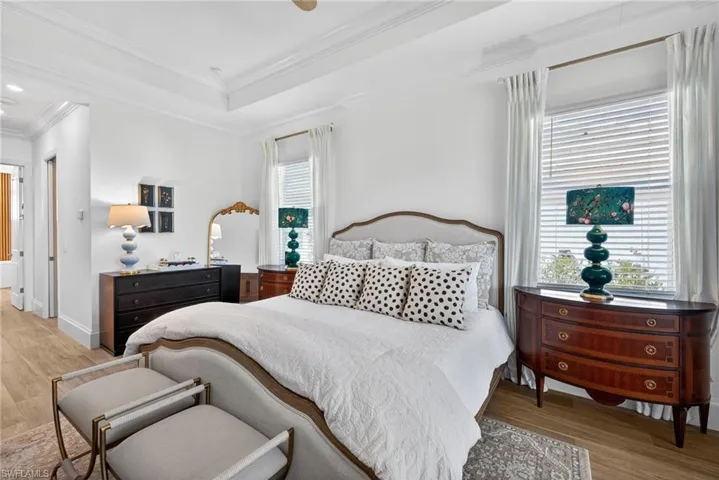 Bedroom featuring light wood-style flooring, a raised ceiling, crown molding, and ceiling fan
