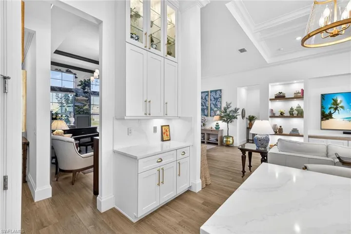 Kitchen featuring crown molding, open floor plan, light stone countertops, white cabinets, and glass fronted cabinets
