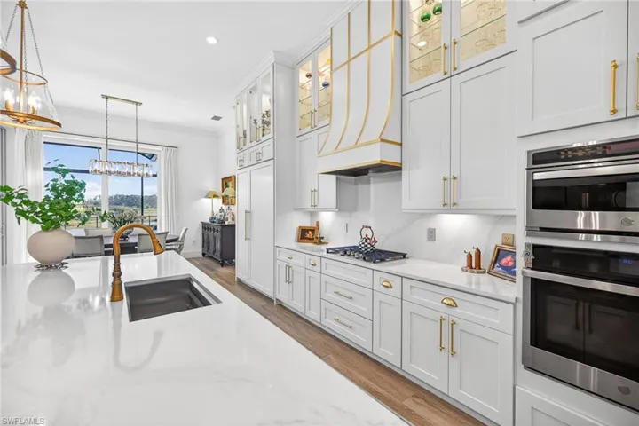 Kitchen featuring stainless steel appliances, crown molding, glass fronted cabinets, white cabinets, and light stone counters