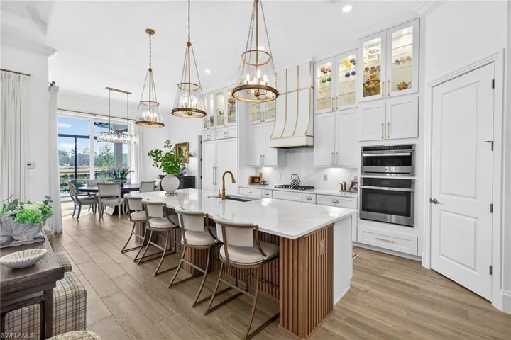 Kitchen with white cabinetry, glass fronted cabinets, a breakfast bar area, an island with sink, and light wood finished floors