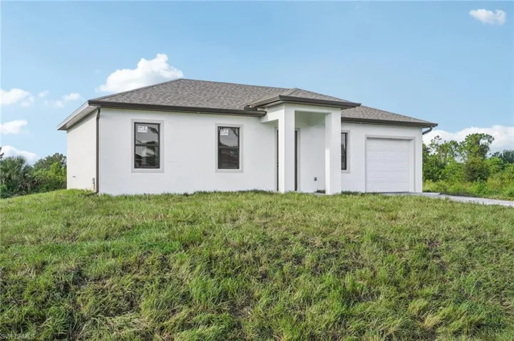 View of front of house featuring an attached garage, stucco siding, a front lawn, and roof with shingles