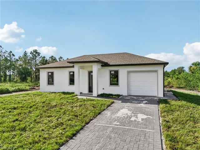 Prairie-style house featuring stucco siding, decorative driveway, a front lawn, a shingled roof, and an attached garage