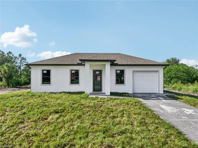 Prairie-style home featuring stucco siding, a front lawn, a shingled roof, an attached garage, and driveway